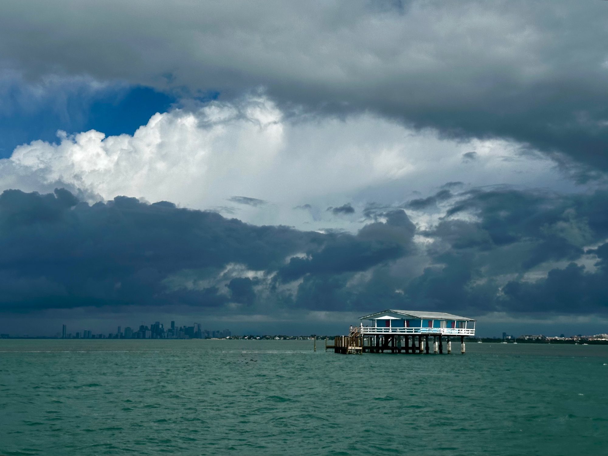 A stilt house on the water with the Miami skyline under storm clouds